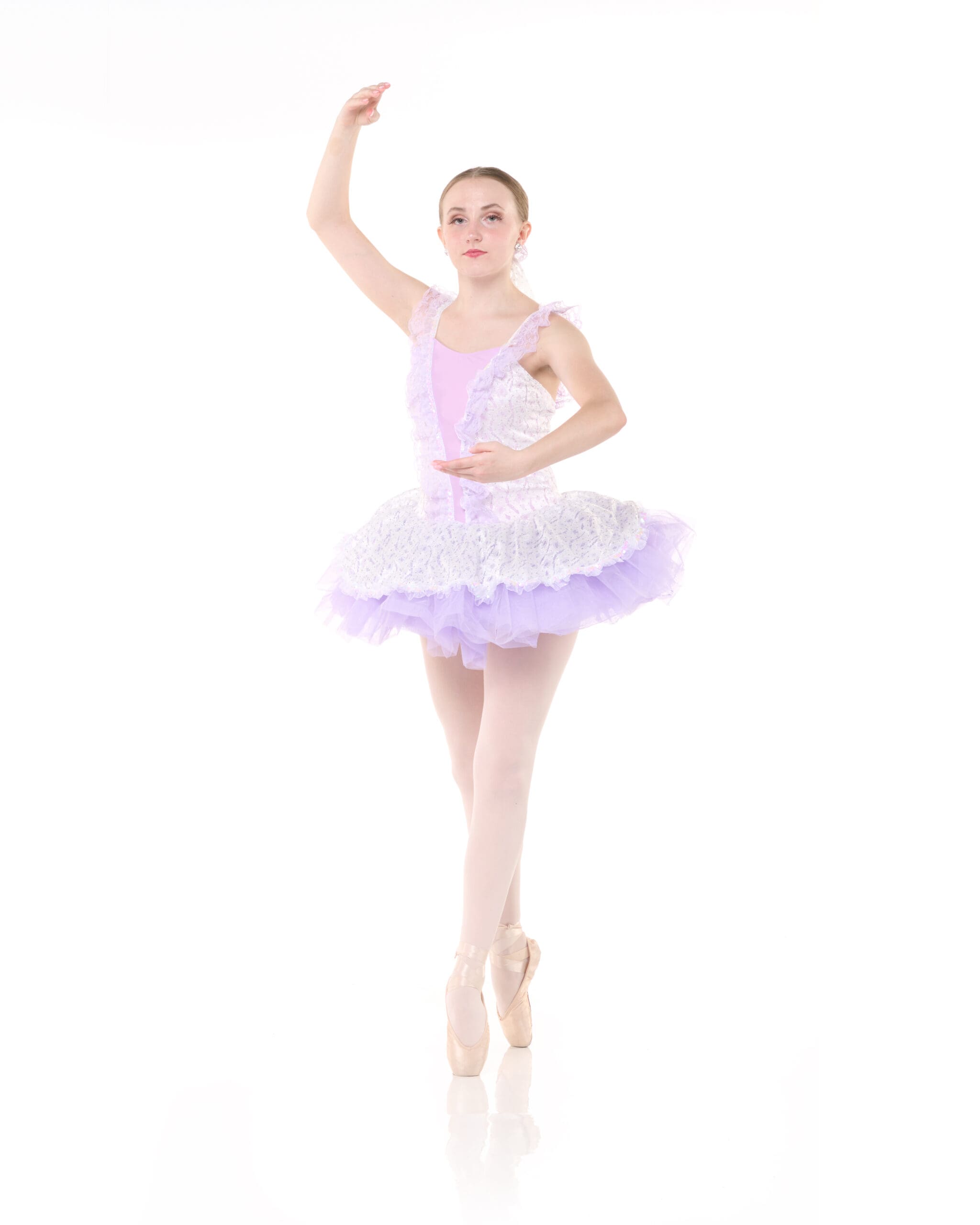 A ballerina in a white and lavender tutu poses on pointe against a white background, with one arm curved above her head and the other resting near her waist.