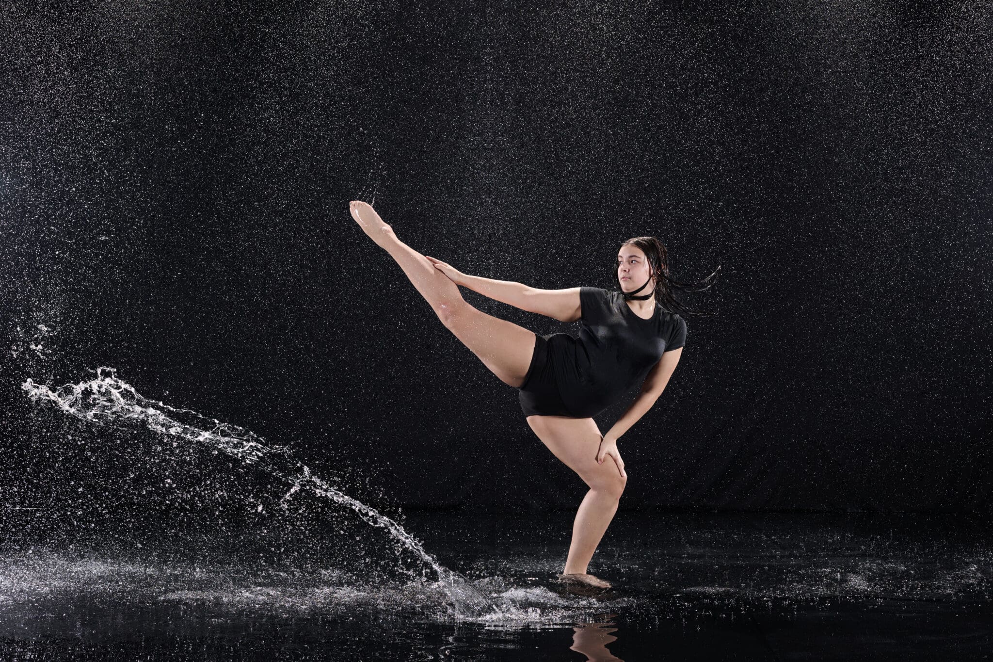 Dancer posing in dramatic rain with bold studio lighting