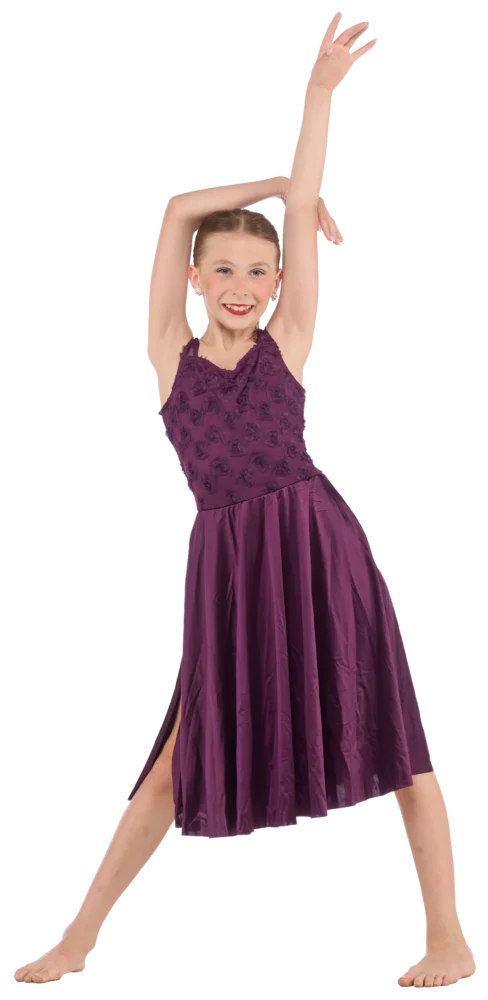 Young girl in a sleeveless purple dress stands barefoot, smiling with one arm raised and the other bent above her head, posing confidently against a white background.